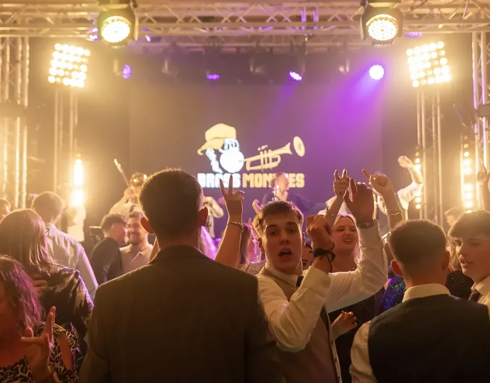 Brass Monkees playing a corporate party on a stage with lighting and PA, guests dancing at the front