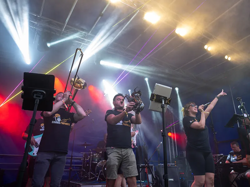 Brass Monkees trombone player and singer on an outdoor festival stage with lasers and stage lights