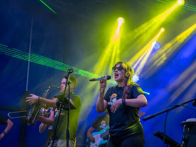 Brass Monkees singer and saxophone player performing under yellow and blue festival stage lights