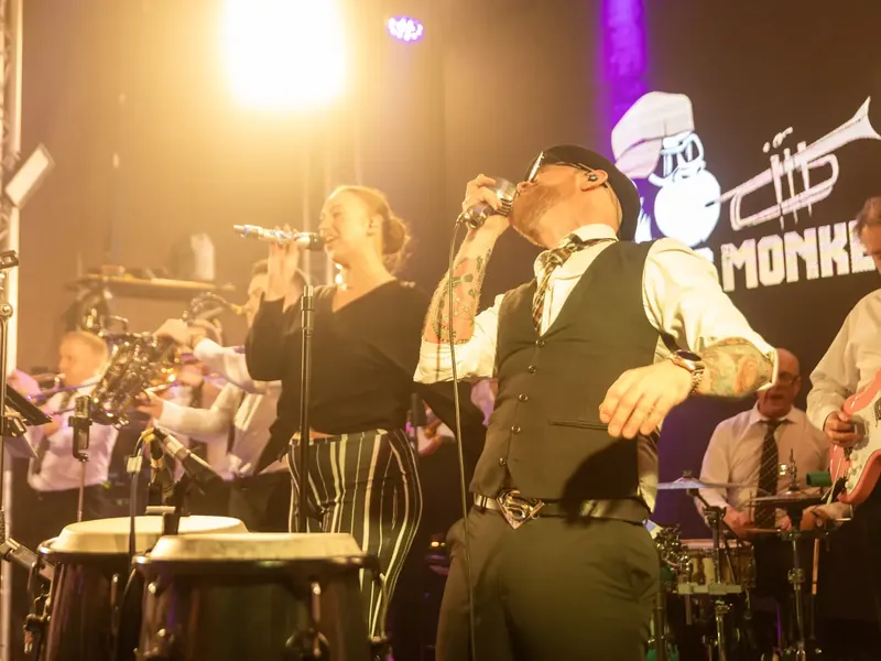Brass Monkees singers performing live to a party crowd in Manchester, with the horns behind