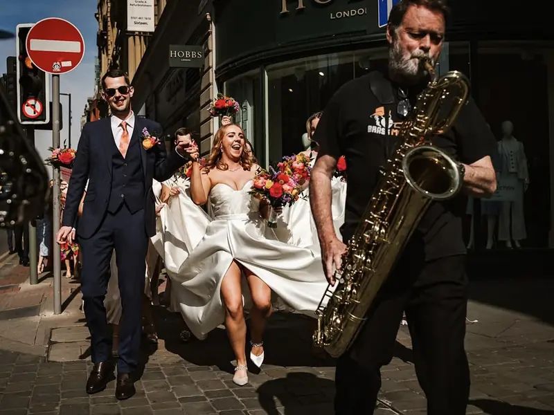 Bride and groom walking with the Brass Monkees roaming brass band saxophonist